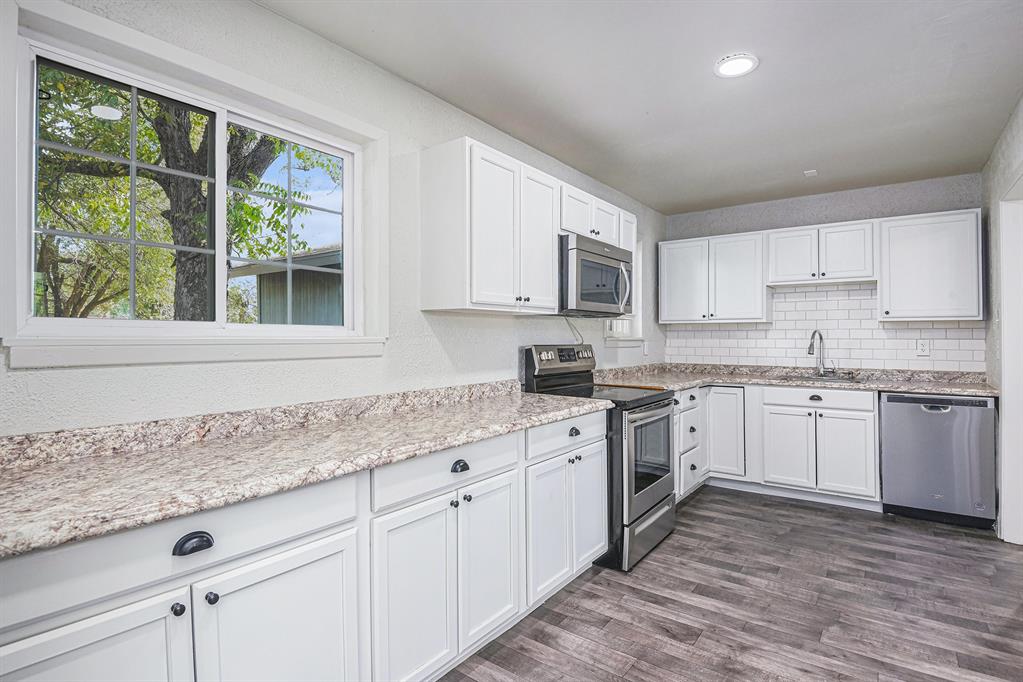 233 Victoria Avenue Azle, TX 76020 - Photo 4 of 25 Kitchen with appliances with stainless steel finishes, tasteful backsplash, white cabinets, dark wood finished floors, and plenty of natural light