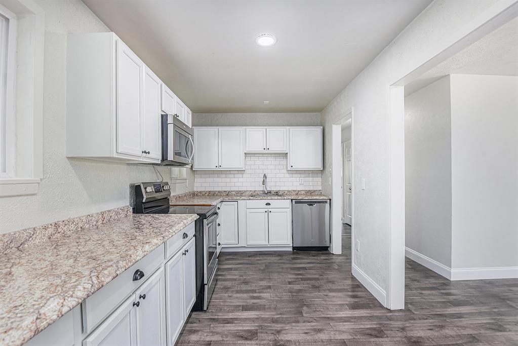233 Victoria Avenue Azle, TX 76020 - Photo 5 of 25 Kitchen with stainless steel appliances, white cabinetry, backsplash, dark wood finished floors, and light stone countertops