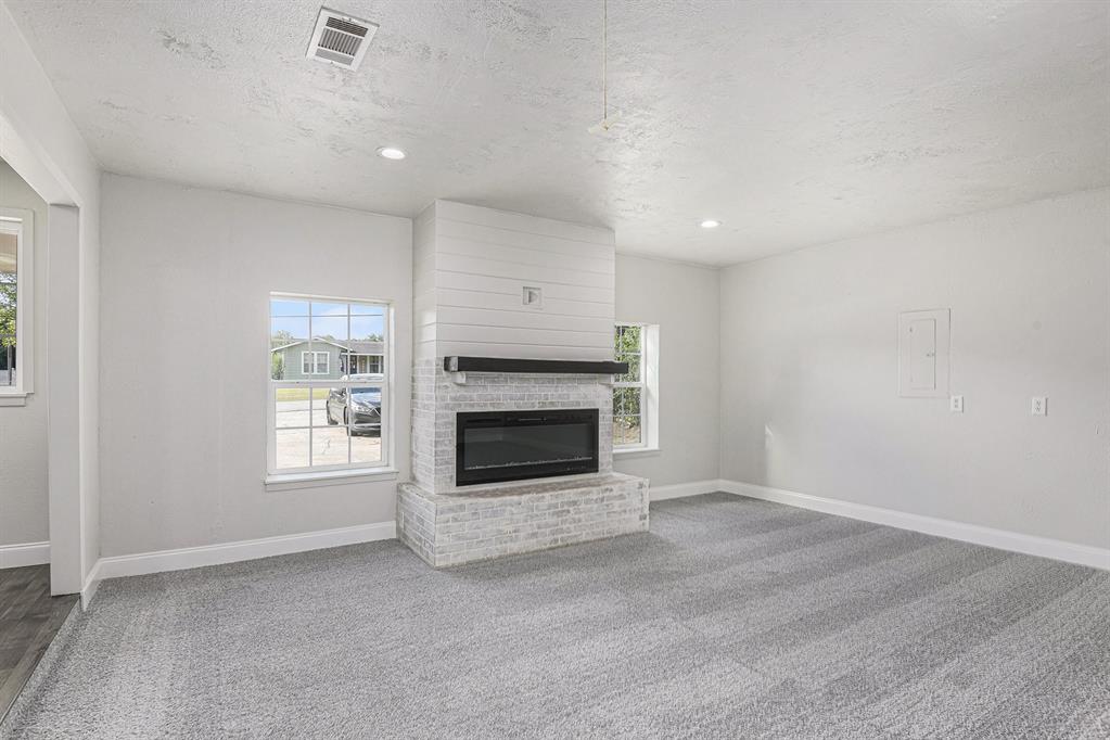 233 Victoria Avenue Azle, TX 76020 - Photo 9 of 25 Unfurnished living room featuring light colored carpet, a textured ceiling, a brick fireplace, recessed lighting, and electric panel