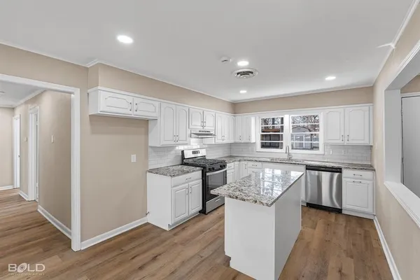 a kitchen with stainless steel appliances granite countertop hardwood floor sink stove and wooden cabinets