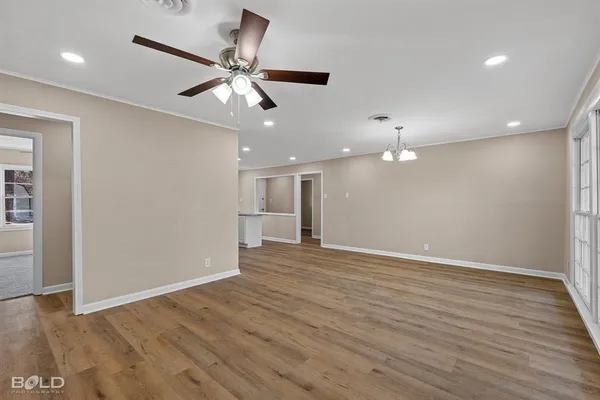 a view of an empty room with wooden floor and a ceiling fan