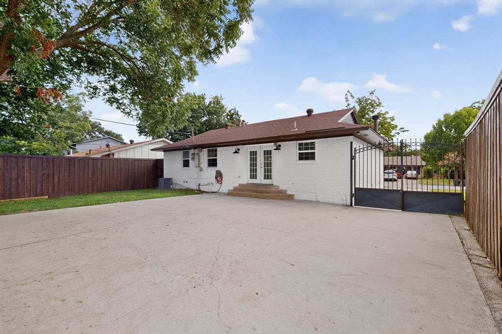 4404 Astor Road Mesquite, TX 75150 - Photo 32 of 38 Expansive concrete patio with white brick exterior, double French doors, a dark wood fence, and a wrought iron gate