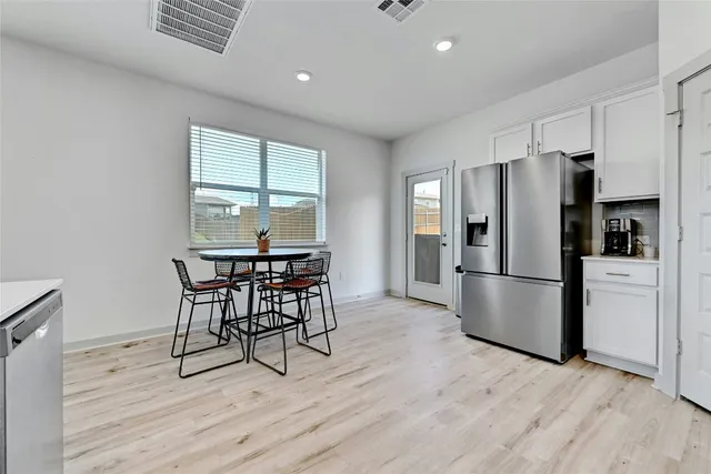 a kitchen with stainless steel appliances a refrigerator a stove a dining table and chairs with wooden floor