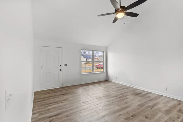 an empty room with wooden floor fan and windows