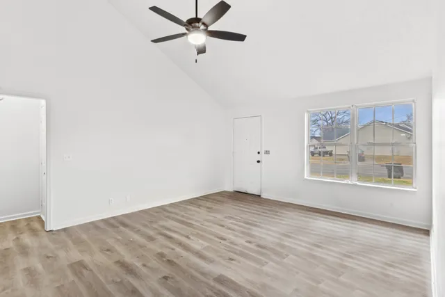 an empty room with wooden floor fan and windows