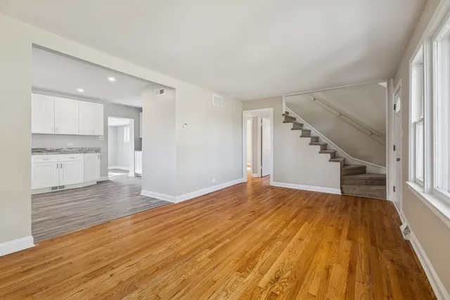 a view of empty room with wooden floor and kitchen