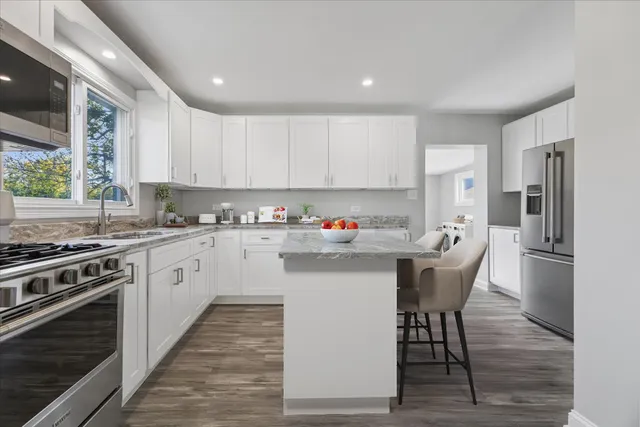 a kitchen with stainless steel appliances kitchen island granite countertop a stove a sink dishwasher a refrigerator and white cabinets with wooden floor
