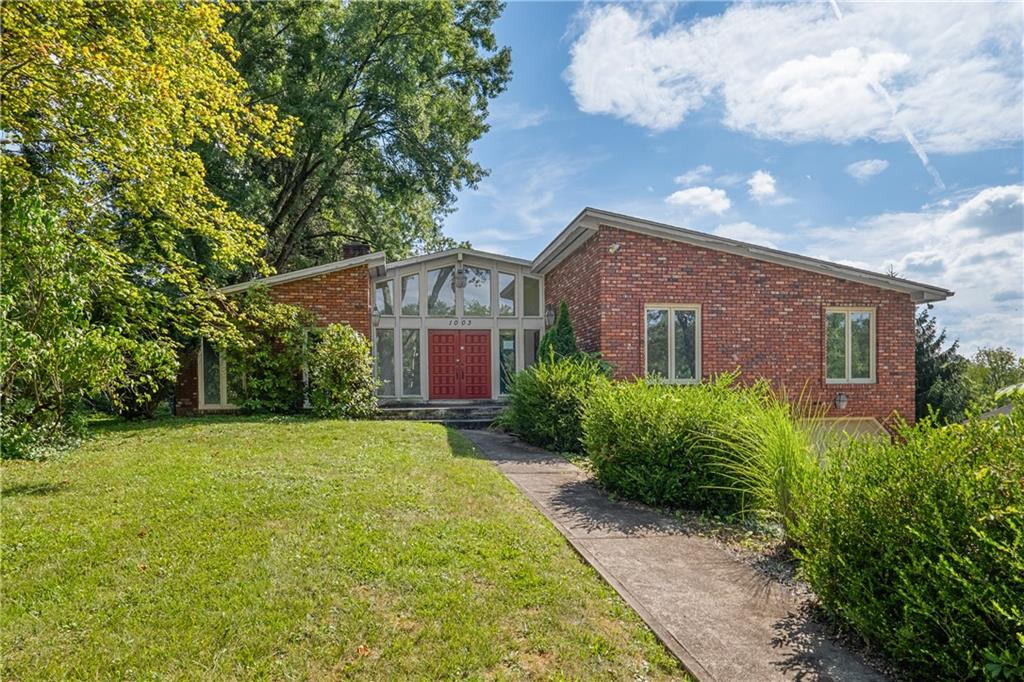 a view of a brick house with a big yard plants and large trees