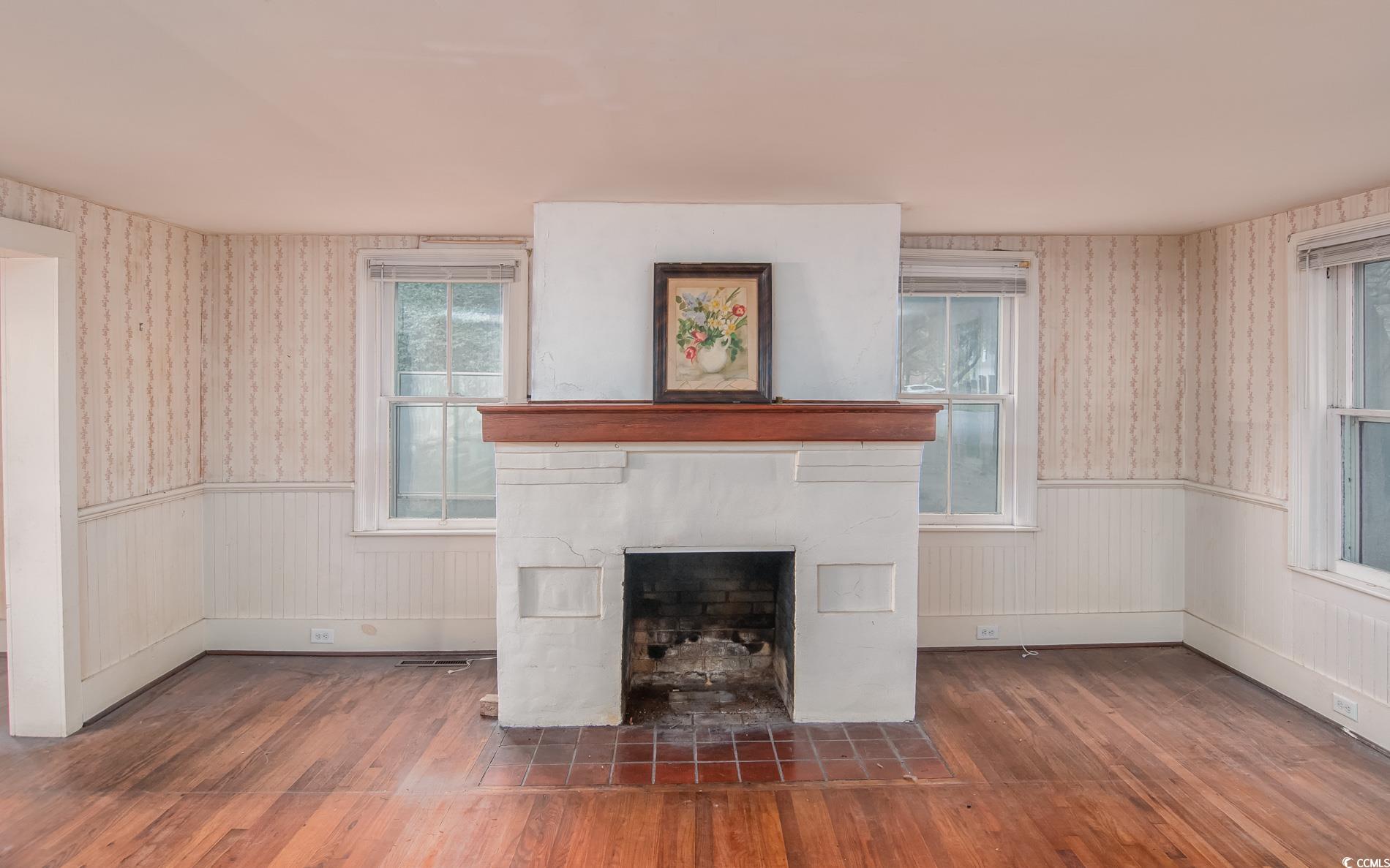 1010 Highmarket Street Georgetown, SC 29440 - Photo 8 of 32 Unfurnished living room featuring wallpapered walls, wood-type flooring, a fireplace with flush hearth, and wainscoting