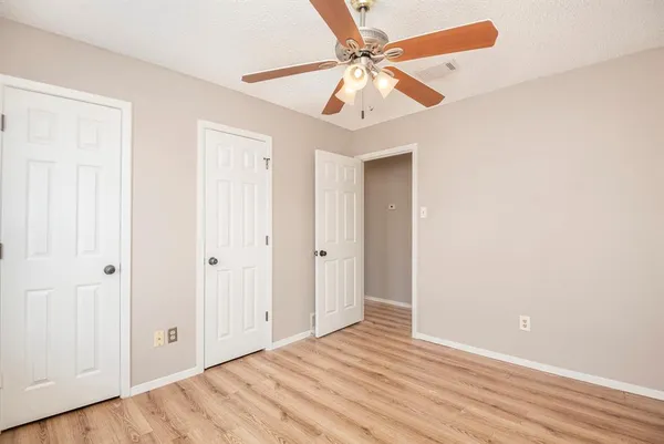 an empty room with wooden floor fan and windows