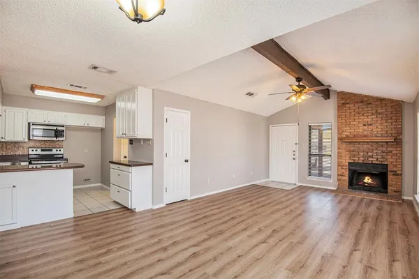 a view of a livingroom with a fireplace wooden floor and kitchen view