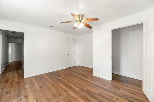 an empty room with wooden floor ceiling fan and windows