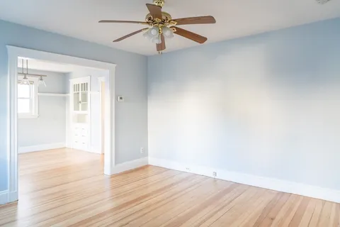 an empty room with wooden floor fan and windows