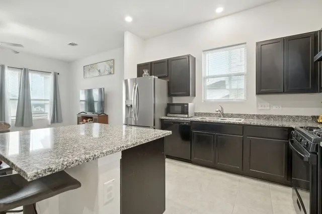a kitchen with stainless steel appliances kitchen island granite countertop a refrigerator a stove a sink counter tops and chairs with wooden floor