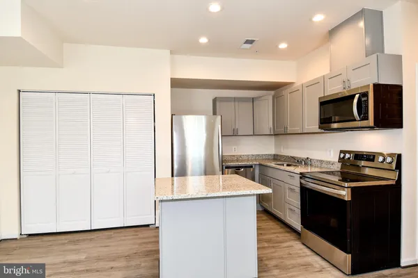 a kitchen with stainless steel appliances a stove top oven a sink a refrigerator white cabinets and wooden floor