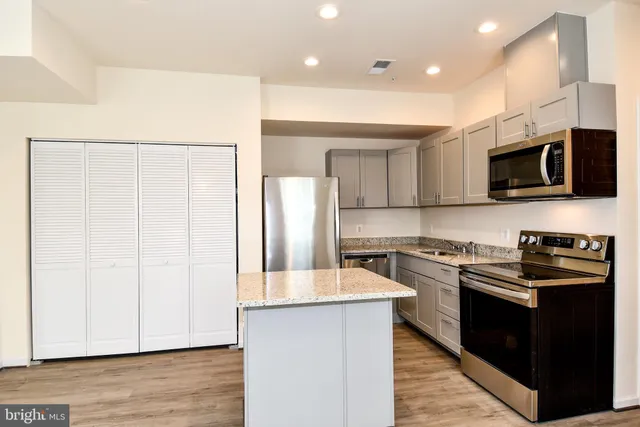 a kitchen with stainless steel appliances a stove top oven a sink a refrigerator white cabinets and wooden floor