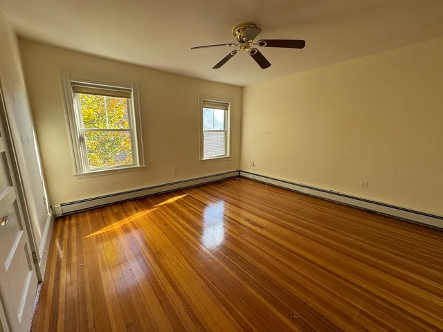 a view of empty room with wooden floor and fan