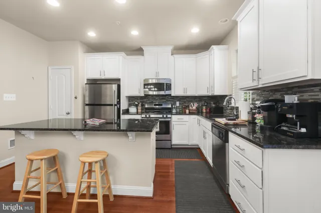 a kitchen with stainless steel appliances granite countertop a stove top oven a sink a refrigerator and white cabinets