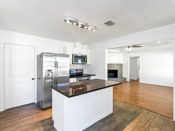 a kitchen with granite countertop a refrigerator oven a sink dishwasher and white cabinets with wooden floor