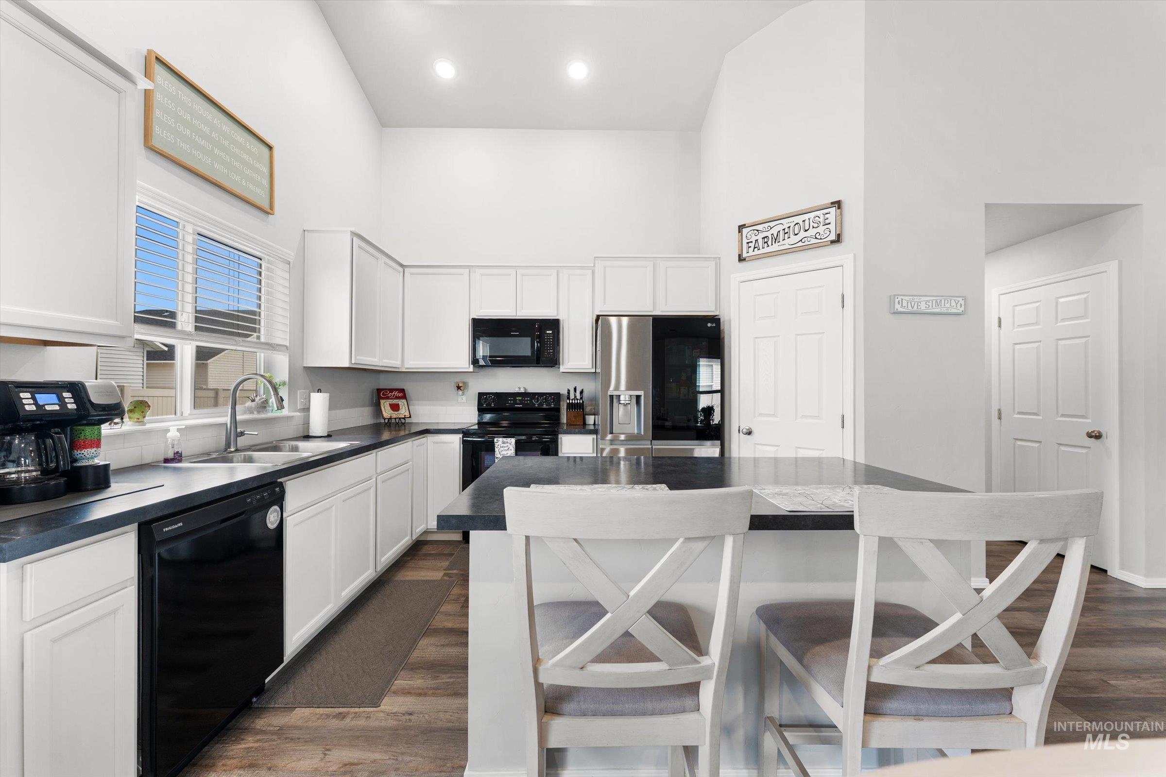 12798 Devonshire Street Caldwell, ID 83607 - Photo 14 of 42 Kitchen featuring dark countertops, a breakfast bar area, white cabinets, black appliances, and a high ceiling