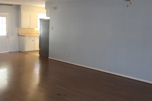 a view of an empty room with wooden floor and fan