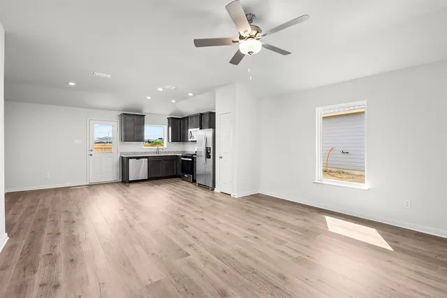 a view of kitchen and empty room with wooden floor and window