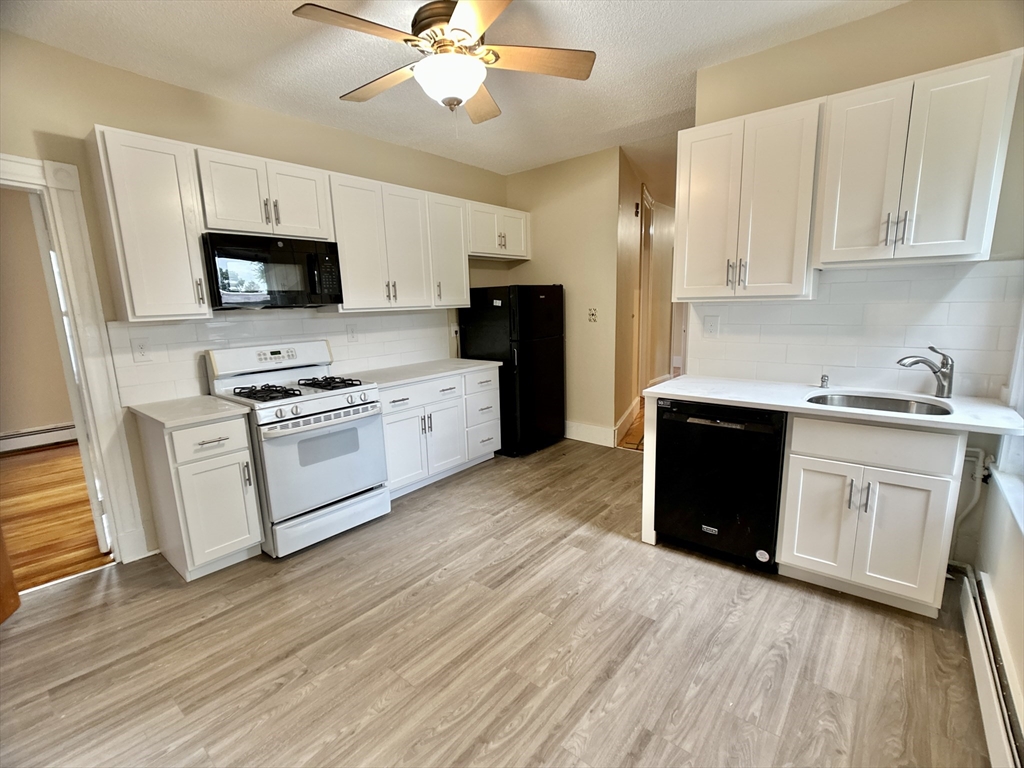 22 Spring Park Avenue, Unit 3 Boston, MA 02130 - Photo 1 of 11 a kitchen with stainless steel appliances white cabinets a sink a stove a refrigerator and microwave with wooden floor