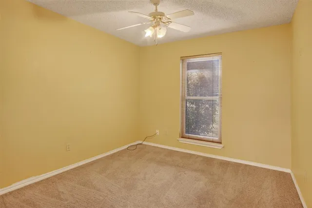 an empty room with chandelier fan and windows