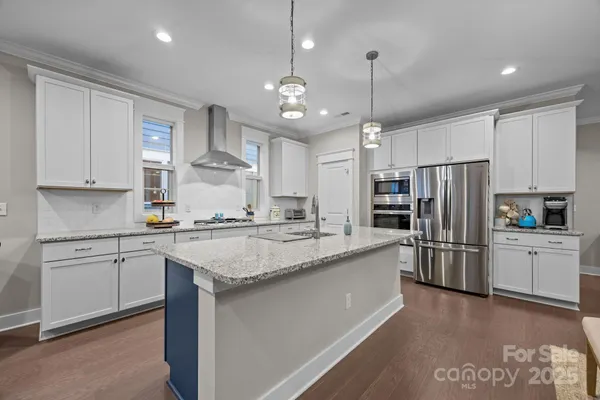 a kitchen with stainless steel appliances granite countertop a sink stove a refrigerator and white cabinets with wooden floor