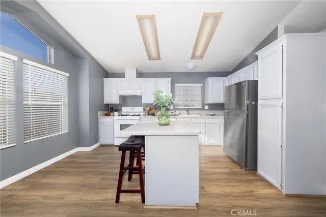 a kitchen with stainless steel appliances kitchen island granite countertop a refrigerator a sink dishwasher a stove a refrigerator and white cabinets with wooden floor