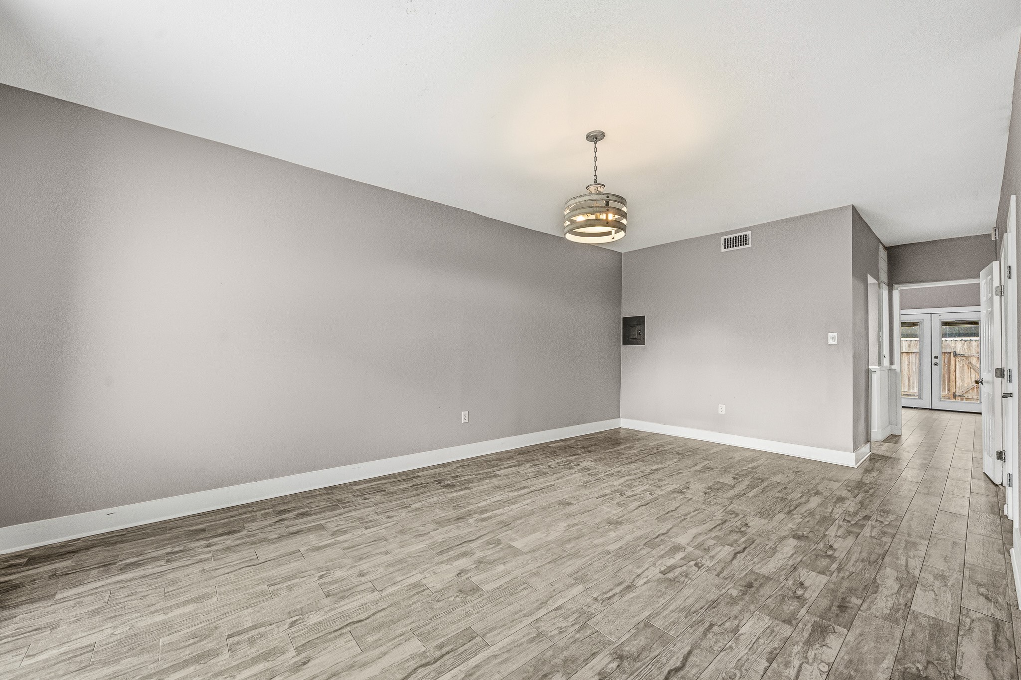 830 Threadneedle Street, Unit 240 Houston, TX 77079 - Photo 6 of 33 This room features a spacious, open layout with neutral gray walls and wood-look tile flooring. It includes a modern pendant light fixture and leads to a door with access to the outdoors. Perfect for a versatile living or dining area.