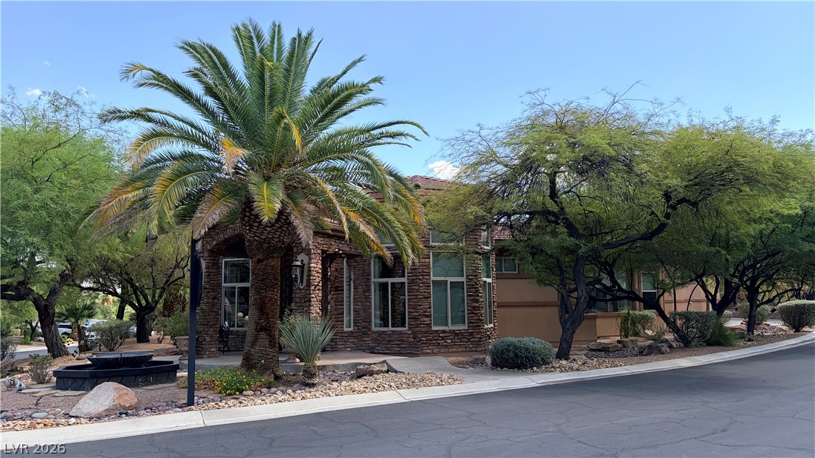 490 Toucan Ridge Court Henderson, NV 89012 - Photo 1 of 7 Mature palms and desert trees frame a striking stone exterior with tall windows.