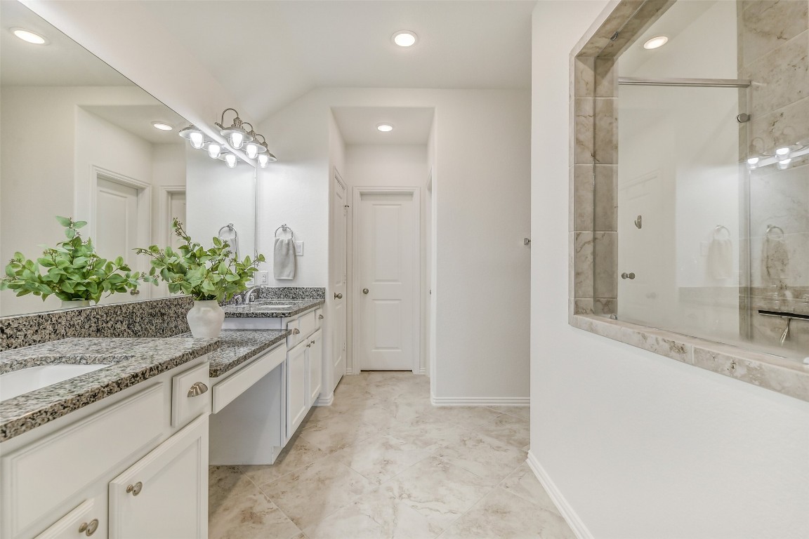 29519 Crimson Beech Drive Spring, TX 77386 - Photo 12 of 22 This primary bathroom features a spacious layout with a dual-sink granite countertop, elegant cabinetry, and a large mirror. It has a tiled floor and a glass-enclosed shower, creating a modern and luxurious feel.