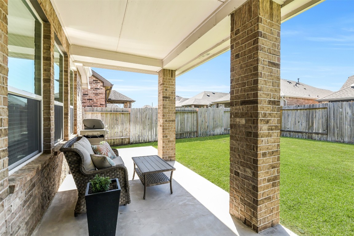 29519 Crimson Beech Drive Spring, TX 77386 - Photo 19 of 22 This photo showcases an extended large covered patio area with brick columns, overlooking a spacious, fenced backyard. It features comfortable seating and a grill, perfect for outdoor relaxation and entertaining.
