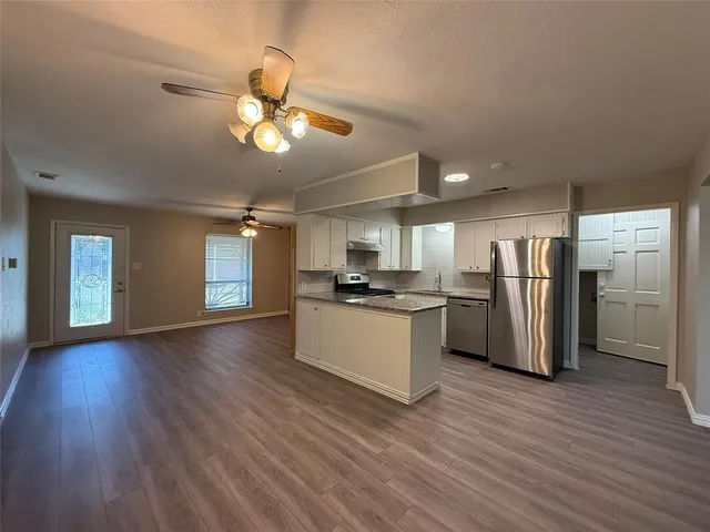 a kitchen with stainless steel appliances granite countertop a refrigerator a sink dishwasher a stove and a refrigerator with wooden floor