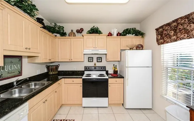 a kitchen with granite countertop a refrigerator sink stove and white cabinets