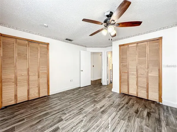 an empty room with wooden floor fan and windows