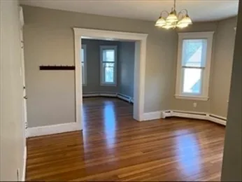 an empty room with wooden floor chandelier and windows