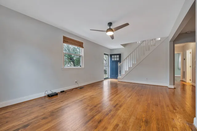an empty room with wooden floor chandelier fan and windows