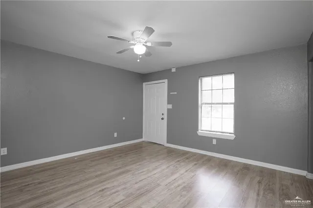 an empty room with wooden floor chandelier fan and windows