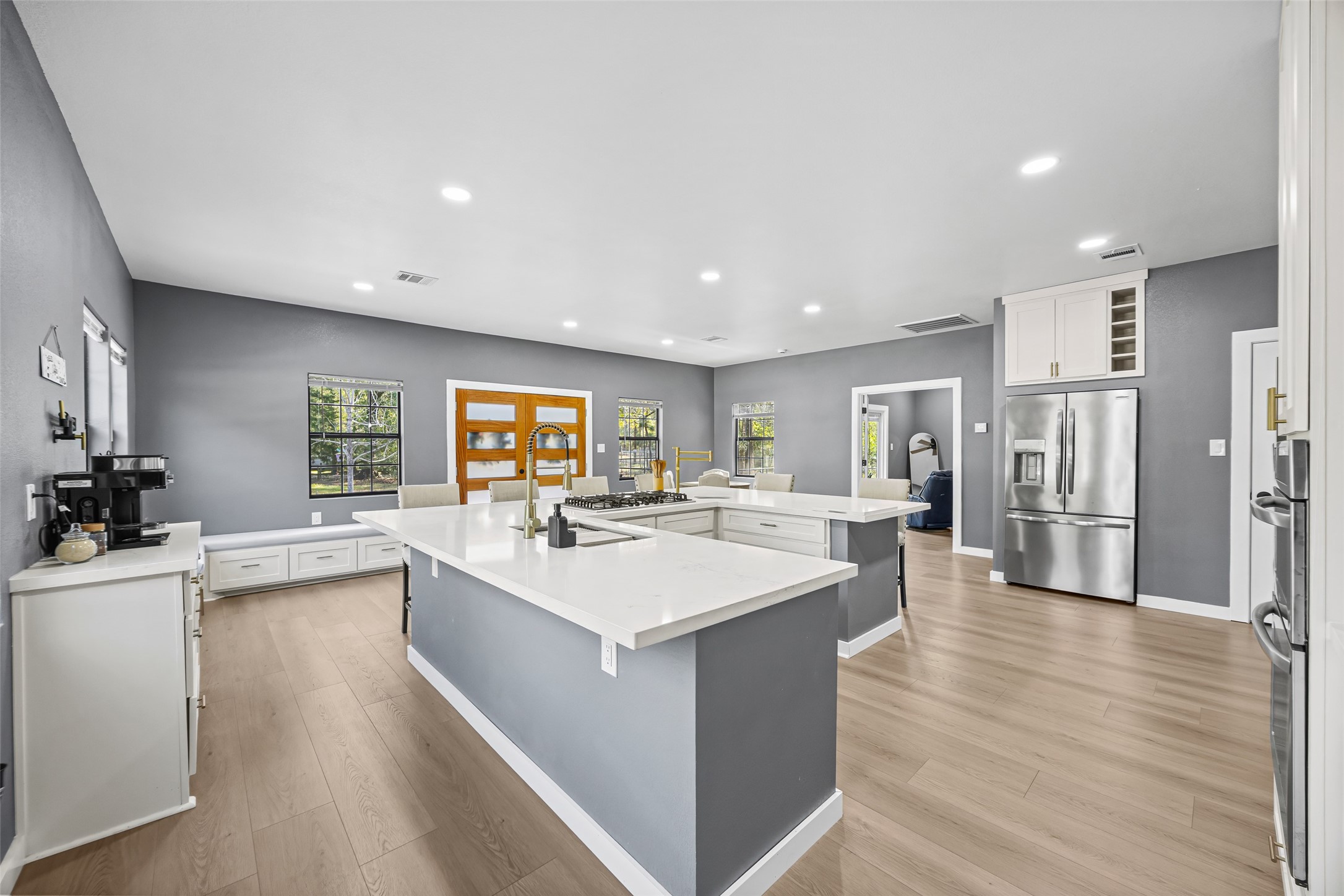 15080 Usher Lane Splendora, TX 77372 - Photo 12 of 44 This kitchen features modern gray walls, ample natural light, and sleek stainless steel appliances. It boasts a large central island with quartz countertops and stylish fixtures, complemented by light wood flooring for a contemporary feel.