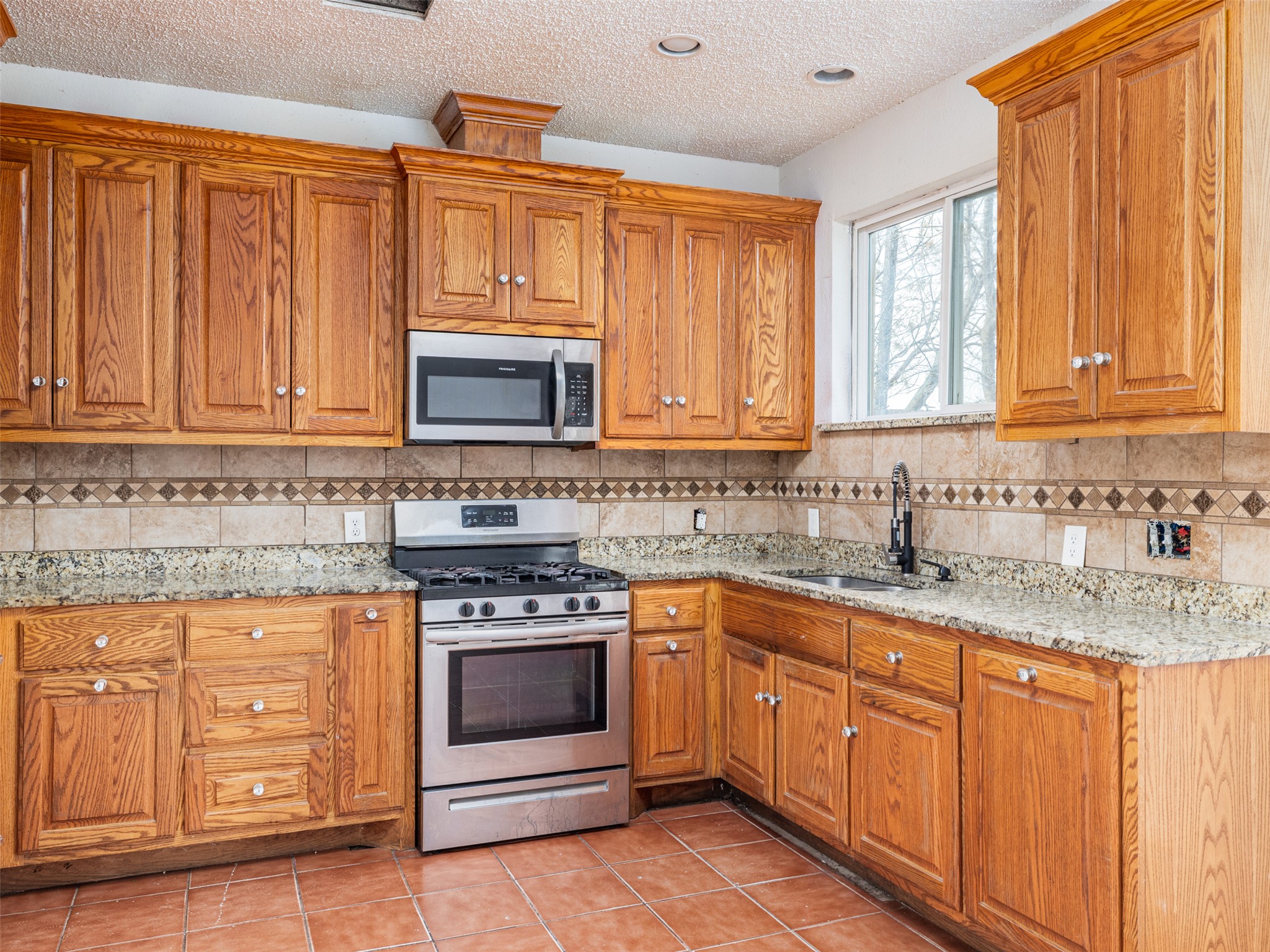 506 Tillery Street Austin, TX 78702 - Photo 4 of 12 Kitchen with stainless steel appliances, light stone countertops, wood finish cabinets, a textured ceiling, and light tile patterned floors