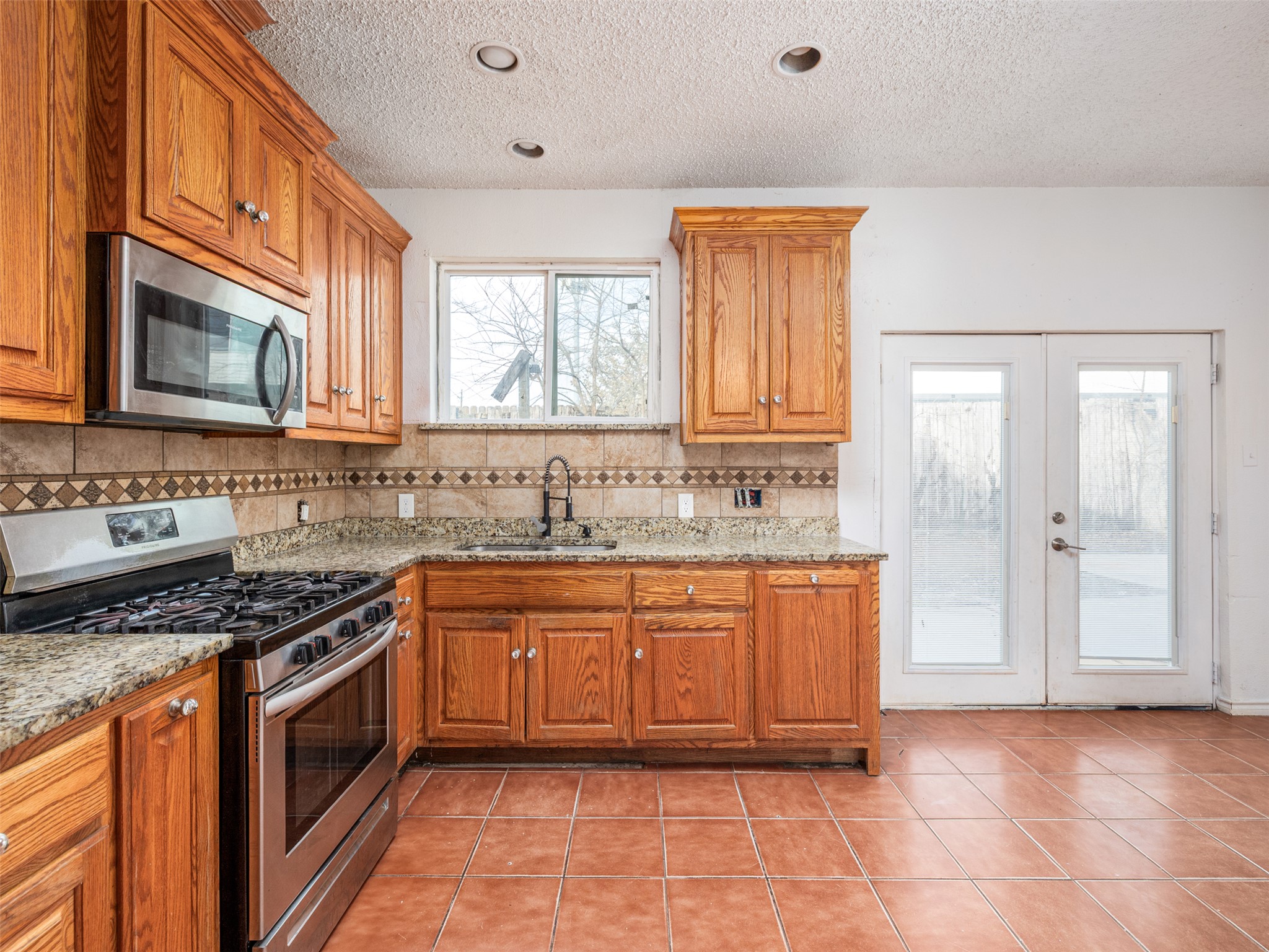 506 Tillery Street Austin, TX 78702 - Photo 5 of 12 Kitchen with stainless steel appliances, french doors, light stone countertops, wood finish cabinetry, and a textured ceiling