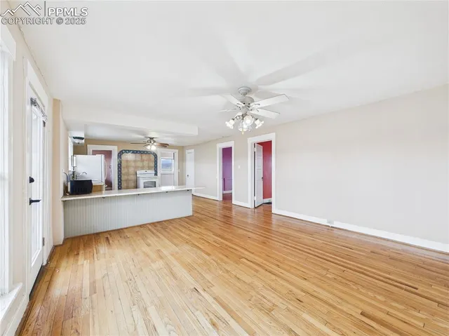 a view of an empty room with wooden floor and a kitchen