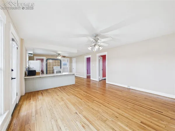 a view of an empty room with wooden floor and a kitchen