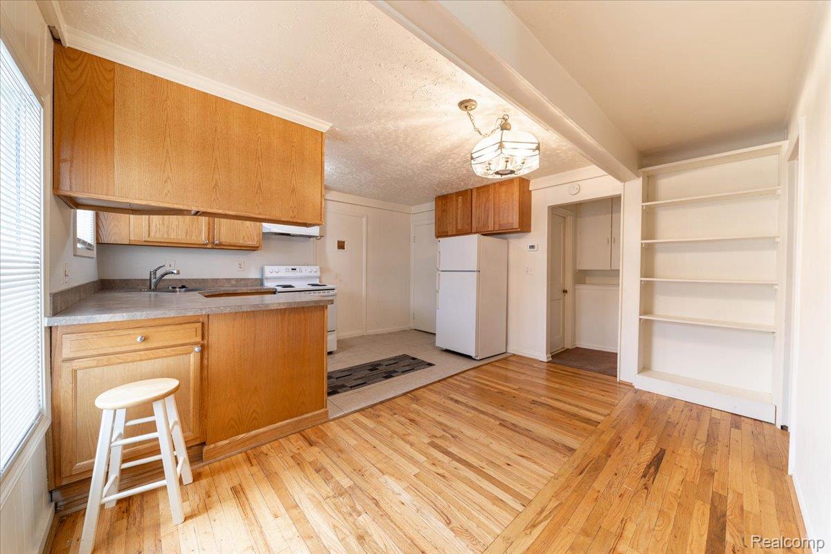 4335 Territorial Road, Unit B Rochester, MI 48306 - Photo 12 of 20 Open-concept living area featuring wood-finish flooring, built-in shelving, and a kitchen with wood cabinetry, a white refrigerator, and a white range