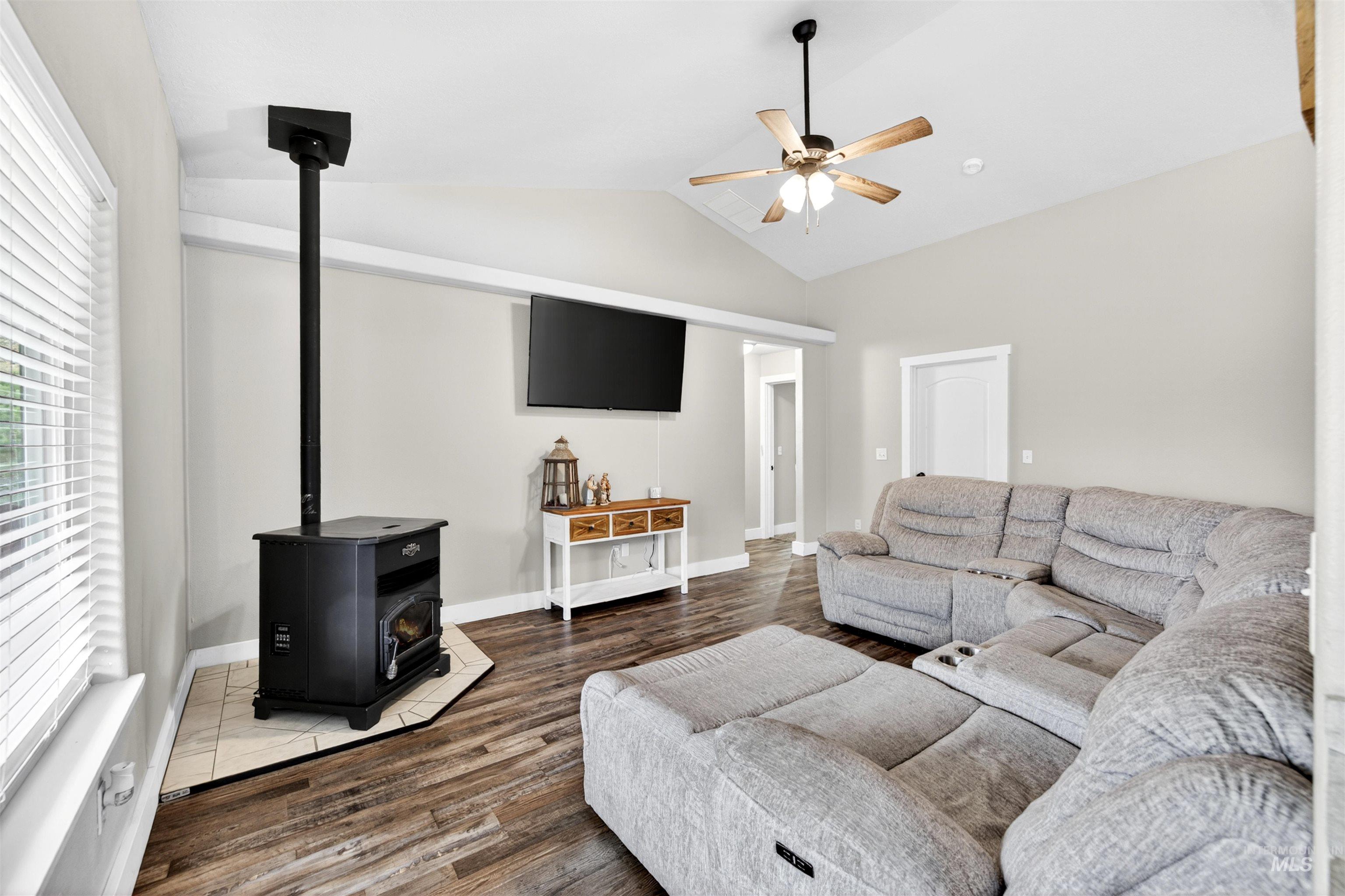 4 Round Up Circle Boise, ID 83716 - Photo 18 of 47 Living area featuring a black corner-set stove on a tiled hearth, wood-finish flooring, vaulted ceiling, and a ceiling fan with integrated lighting