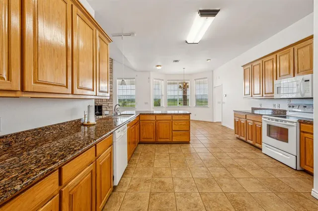 a large kitchen with stainless steel appliances granite countertop a stove a sink dishwasher and microwave with wooden floor