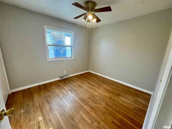 an empty room with wooden floor and chandelier fan