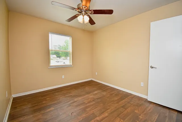 an empty room with wooden floor fan and windows